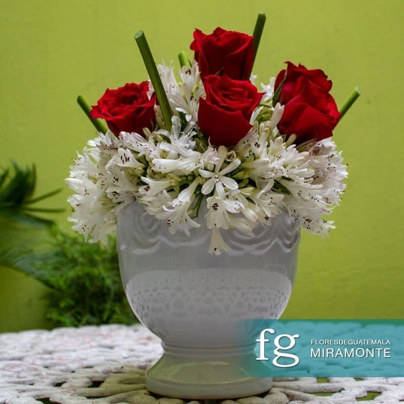 Red roses and white flowers arranged in a white ceramic vase.