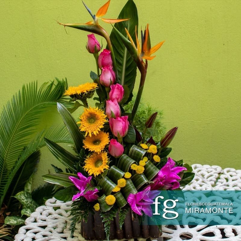 Tall tropical arrangement with roses, sunflowers, lilies, and birds of paradise.